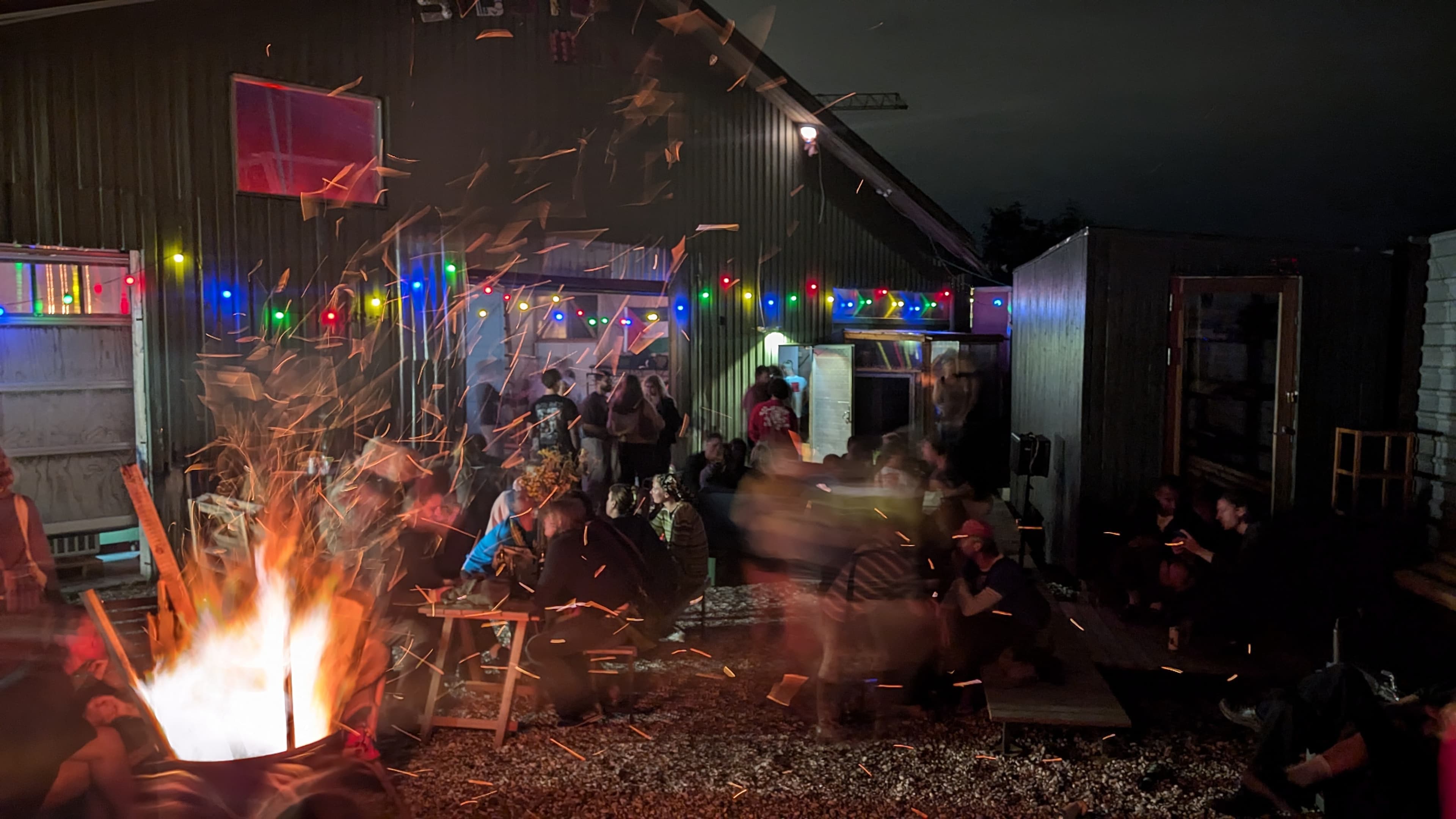 People sitting and talking around a fireplace before the hangar in the summer evening.